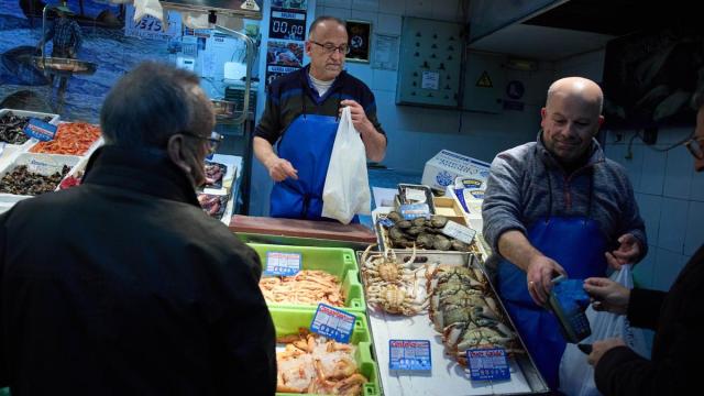 Dos vendedores atienden a los clientes en una pescadería.