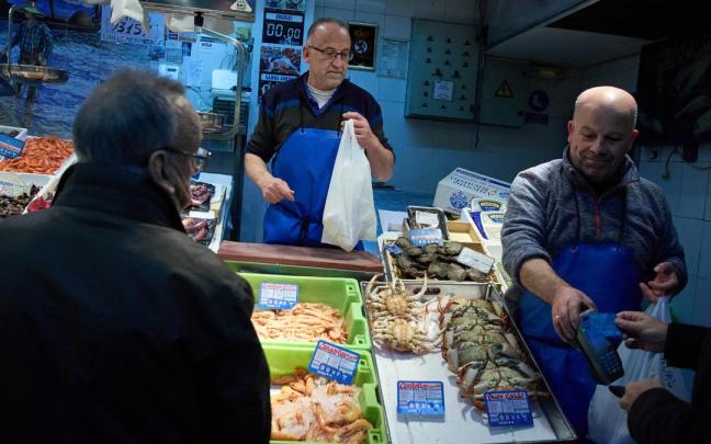 Dos vendedores atienden a los clientes en una pescadería.