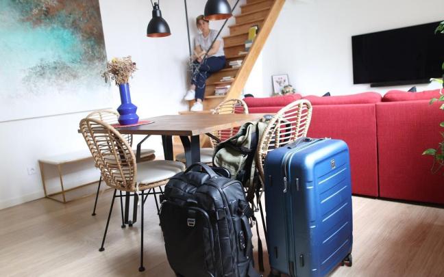 Una viajera, al fondo, en el salón de un apartamento con las maletas en primer plano.