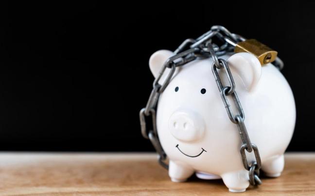 Una hucha con ahorros bloqueada por una cadena y un candado.