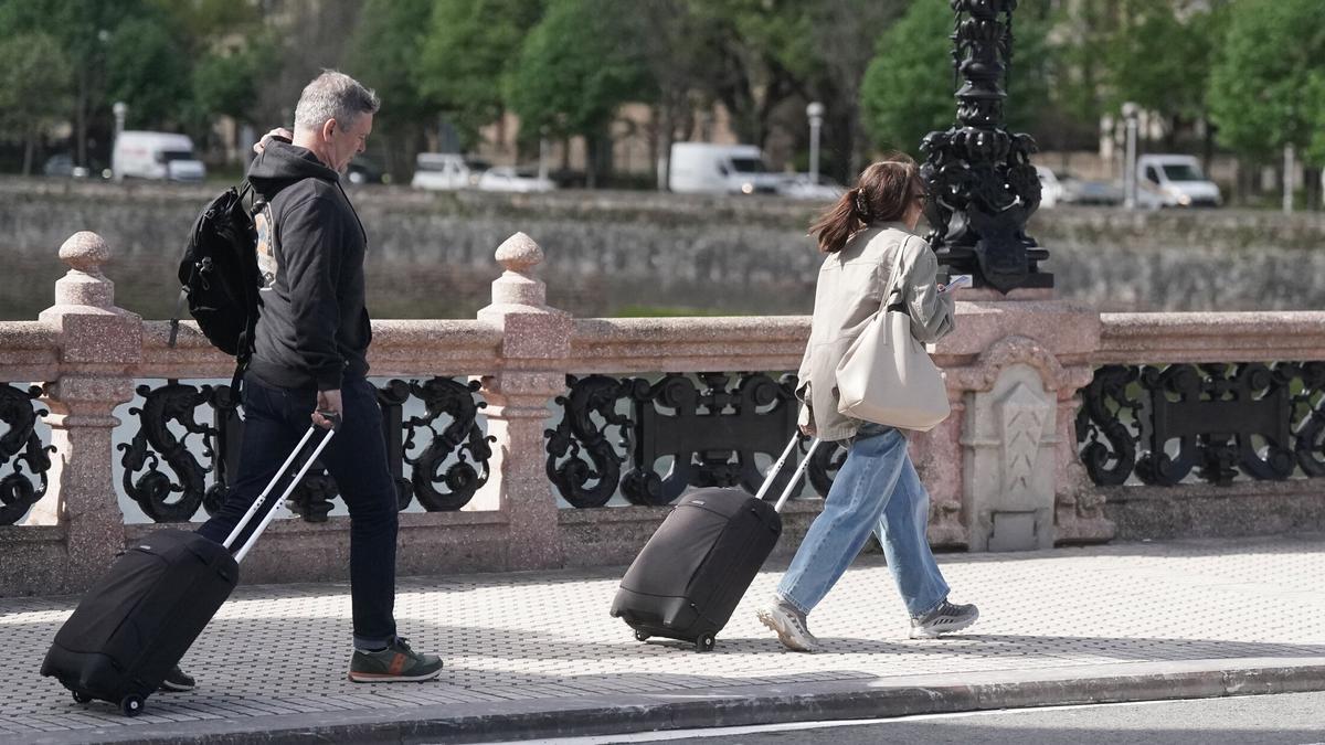Dos turistas caminan con su maleta por el Puente de María Cristina de Donostia. / Ruben Plaza