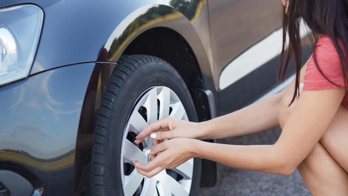 Una joven revisa el estado de un neumático de su coche.