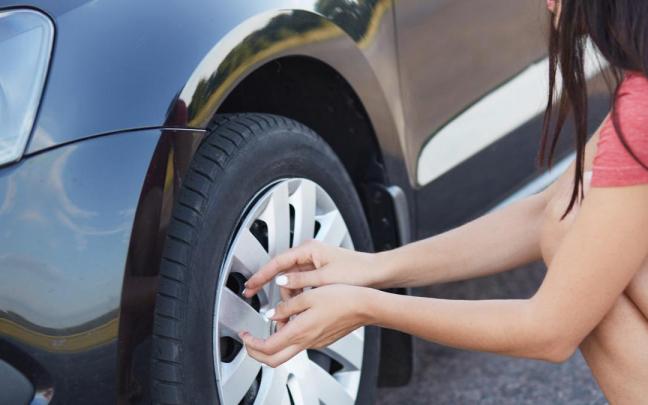 Una joven revisa el estado de un neumático de su coche.