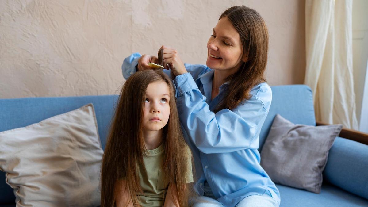 Una mujer pasa la lendrera por el pelo de su hija.