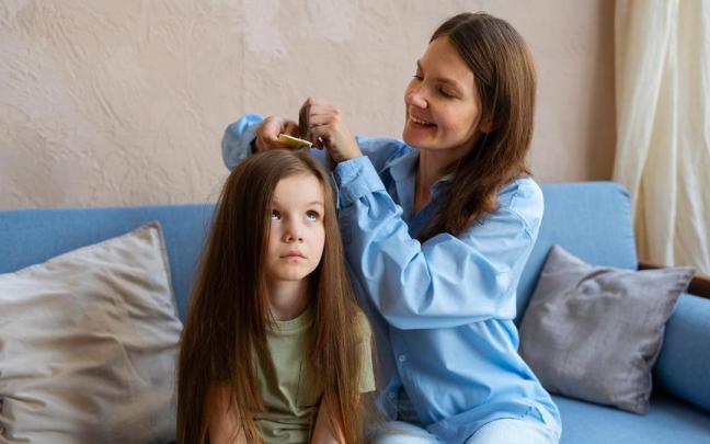 Una mujer pasa la lendrera por el pelo de su hija. Una mujer pasa la lendrera por el pelo de su hija.
