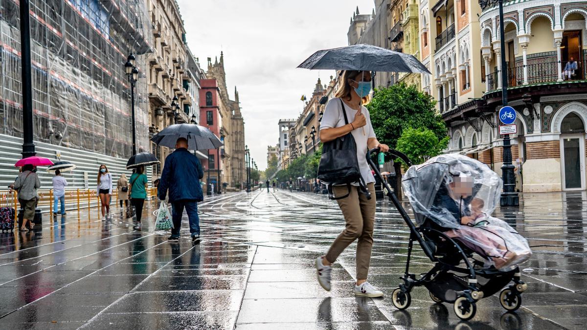 Una madre lleva un carrito de bebé protegido para la lluvia.