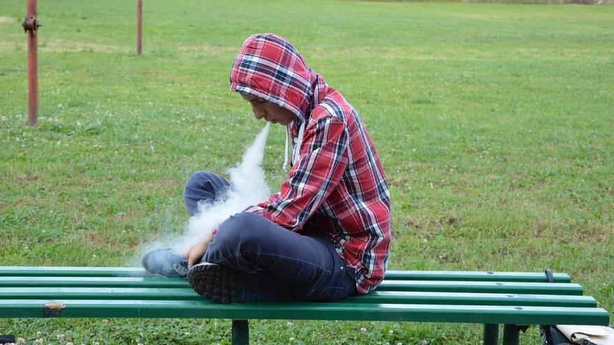 Un joven vapea en el banco de un parque.