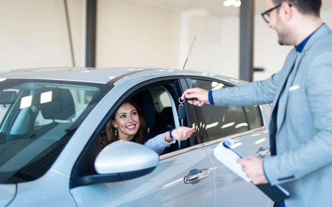 Un trabajador de un concesionario entrega las llaves de un coche a su nueva propietaria.