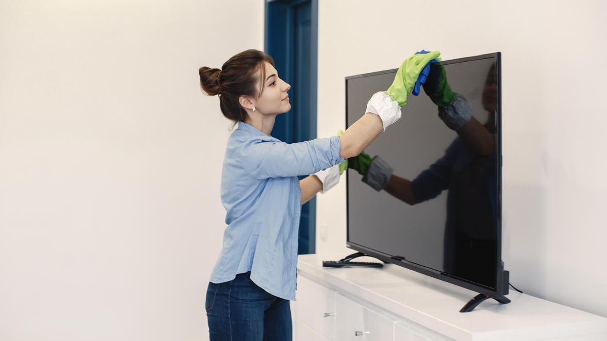 Chica limpia la televisión con cuidado utilizando los productos adecuados y evitando tocar la pantalla con las manos