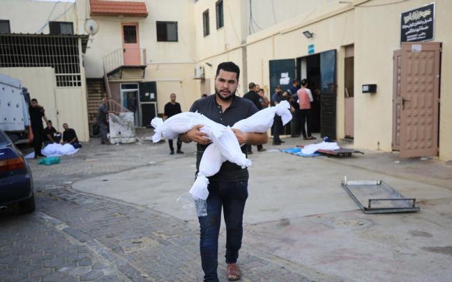 Un hombre carga con los cuerpos de dos menores fallecidos en un ataque israelí en Gaza.