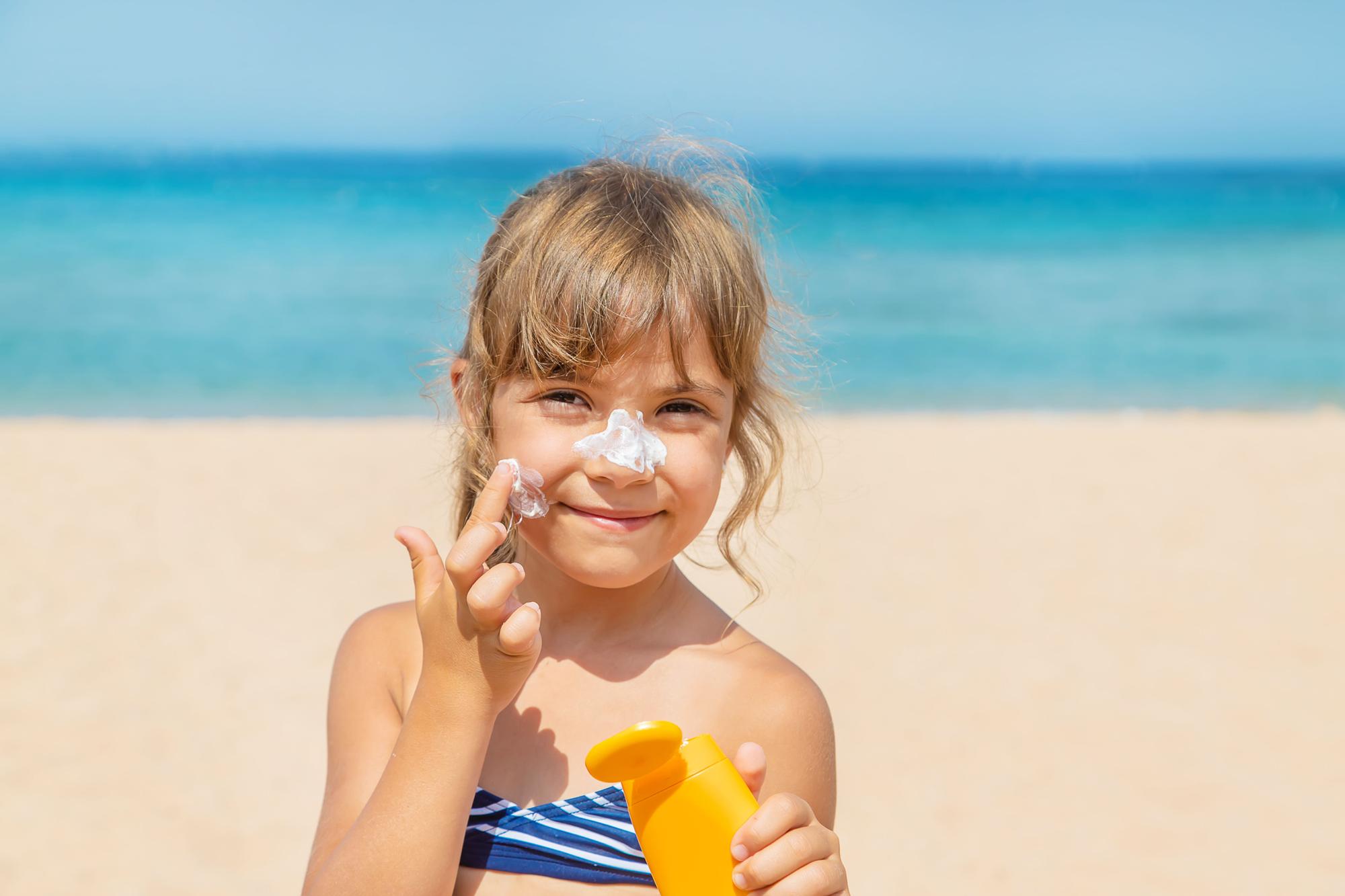 Niña se aplica protector solar en la cara durante un día de playa.