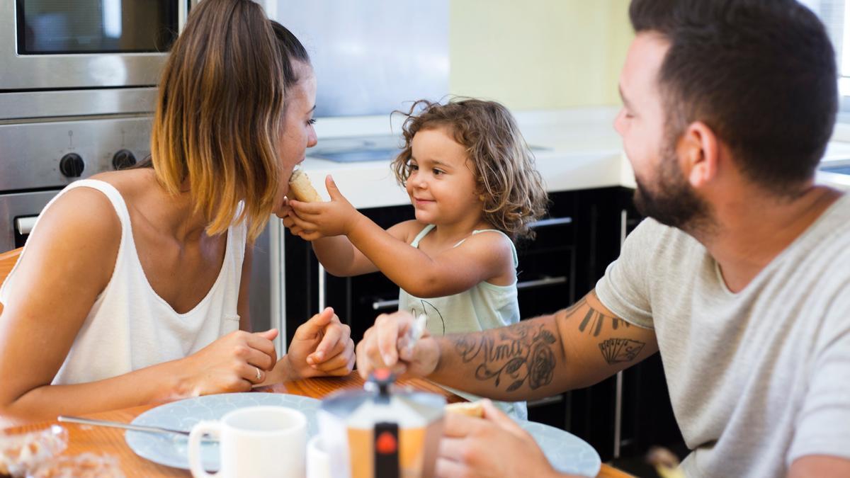 Una pareja joven comparte la hora de comer con su hija en casa.