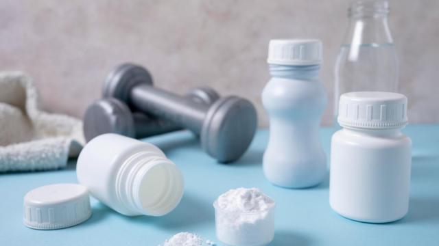 Varios suplementos de creatina con unas mancuernas detrás