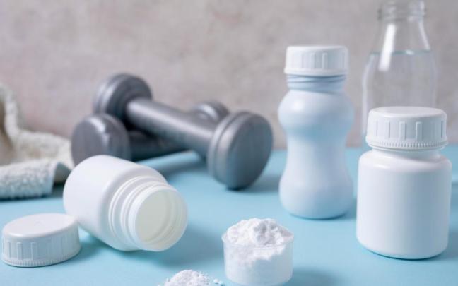Varios suplementos de creatina con unas mancuernas detrás