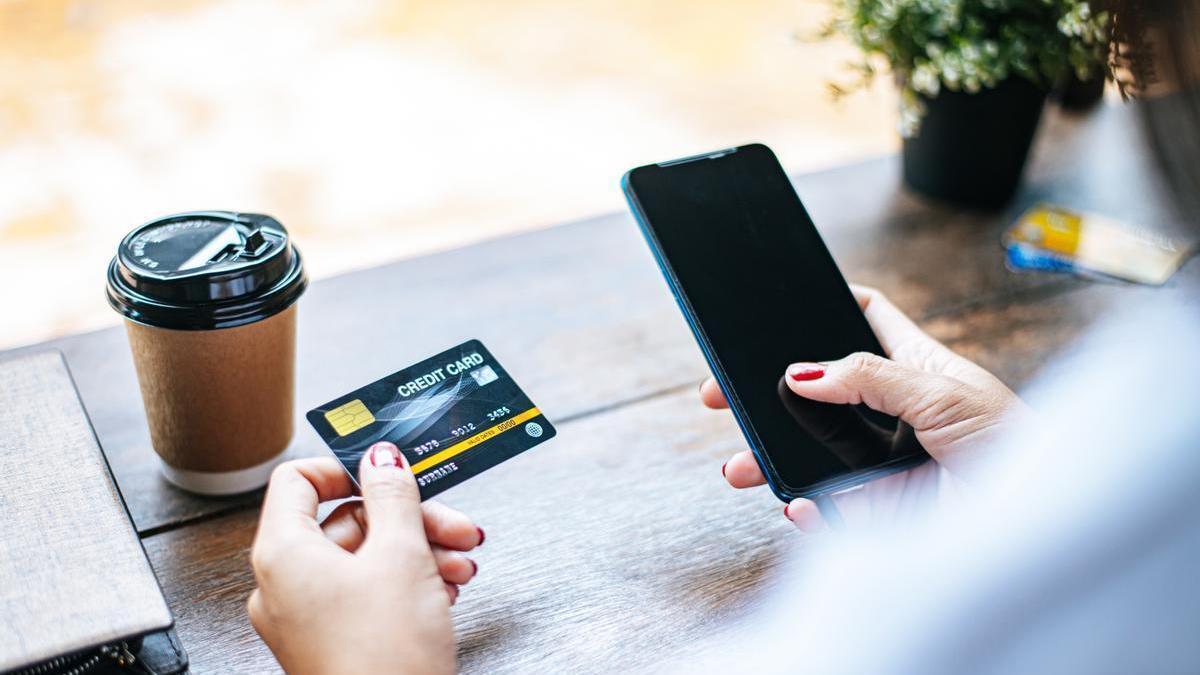 Chica tomando un café en una cafetería mientras consulta sus datos bancarios en el teléfono móvil.