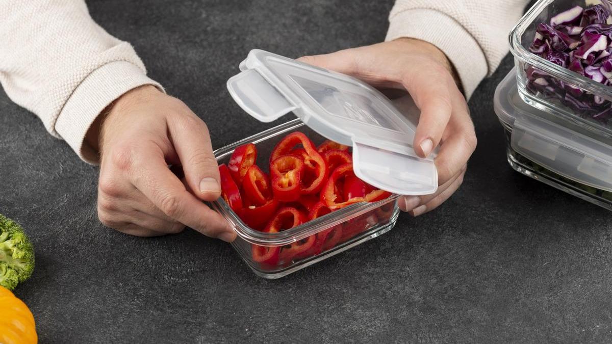 Hombre cierra la tapa de un tupper de cristal con pimientos rojo troceado en su interior