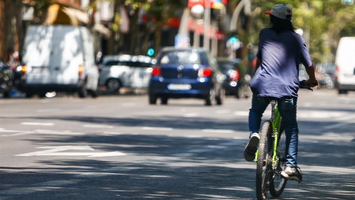 Un hombre cicula en su bicicleta por una calle junto a varios coches.