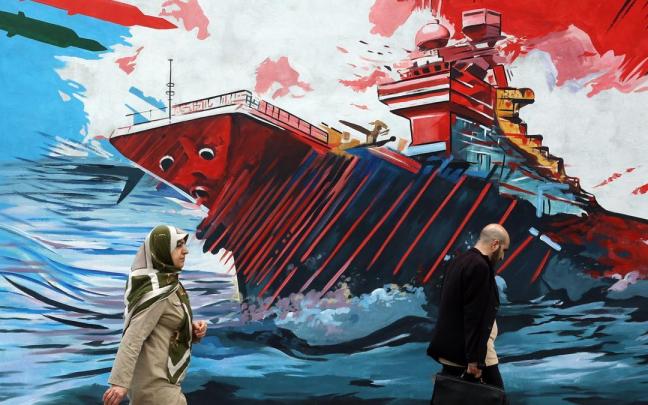 Iraníes pasan junto a un mural contra EE.UU. e Israel en una calle de Teherán