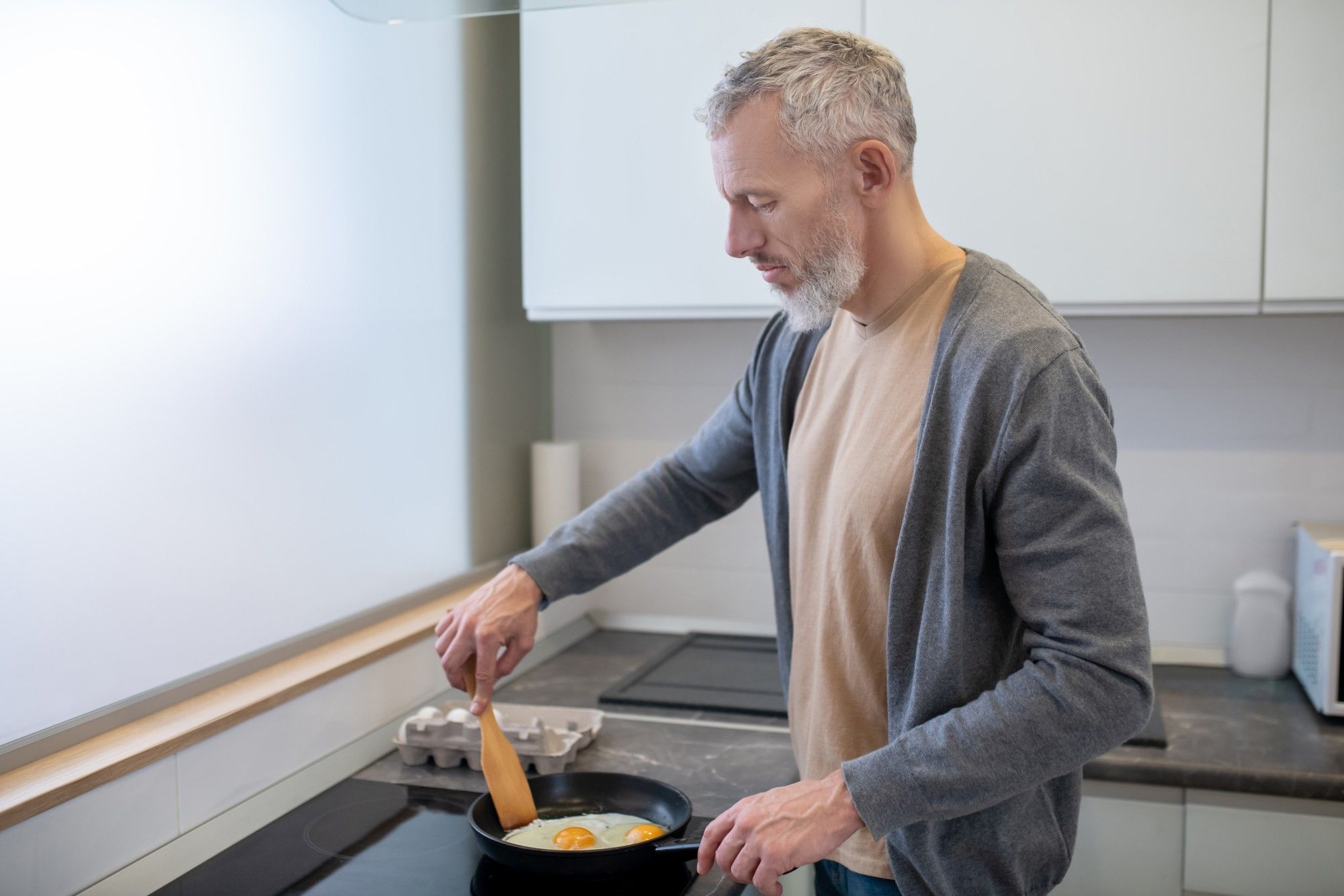 Un hombre cocina huevos fritos en una placa vitrocerámica.