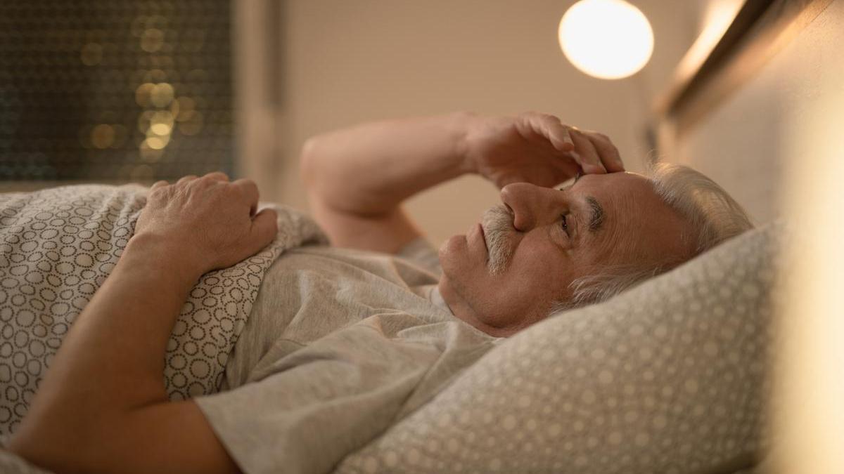 Señor mayor tumbado en la cama con dificultad para conciliar el sueño