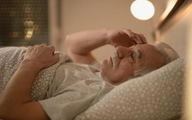 Señor mayor tumbado en la cama con dificultad para conciliar el sueño