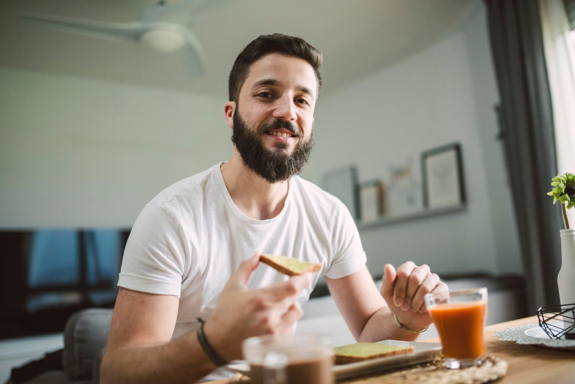 Un hombre desayuna tostadas con mantequilla, zumo y café.