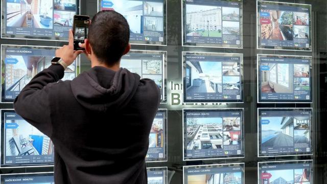 Un joven saca una fotografía a los precios de las viviendas que muestra una inmobiliaria