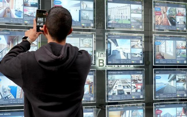 Un joven saca una fotografía a los precios de las viviendas que muestra una inmobiliaria