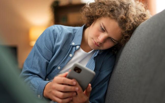 Un adolescente deprimido con el móvil en las manos.