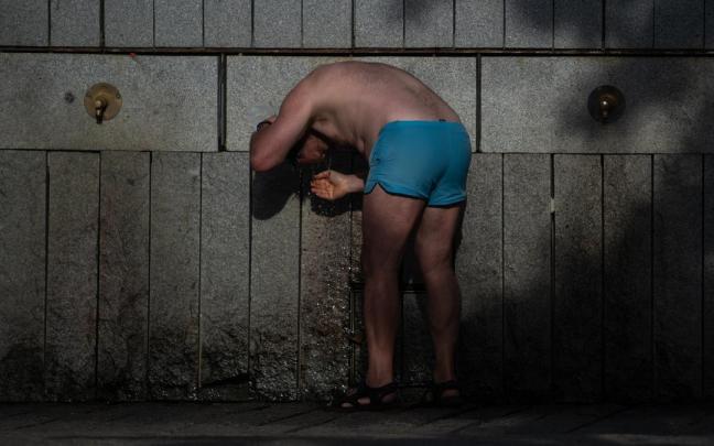 Una persona se refresca en una fuente, en Madrid.