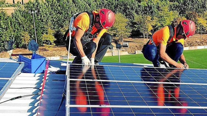 Dos operarios instalan placas solares en una azotea.