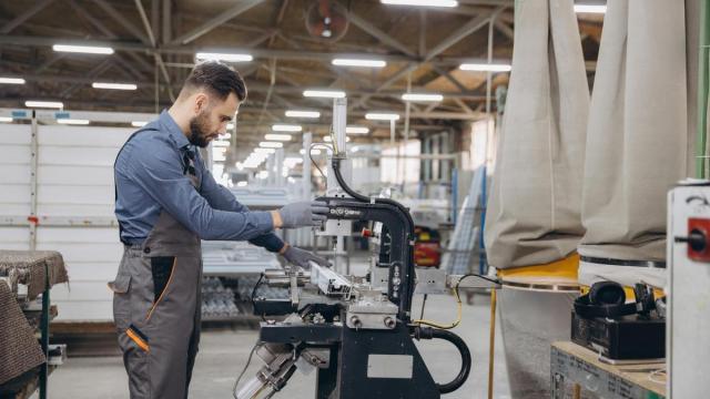 Un trabajador de una fábrica de puertas y ventanas maneja una máquina.