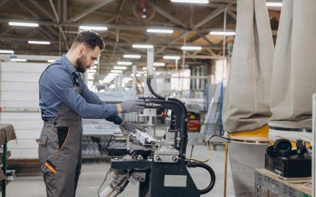 Un trabajador de una fábrica de puertas y ventanas maneja una máquina.