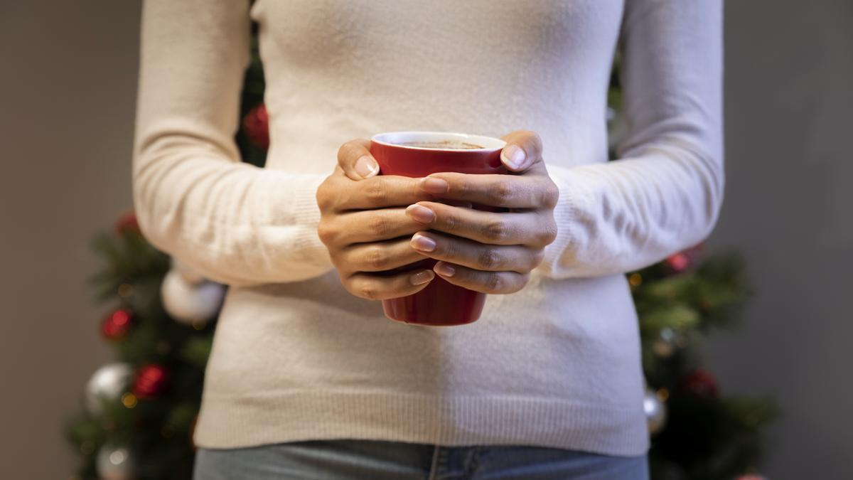 Mujer sostiene una taza con las manos con un árbol de Navidad de fondo