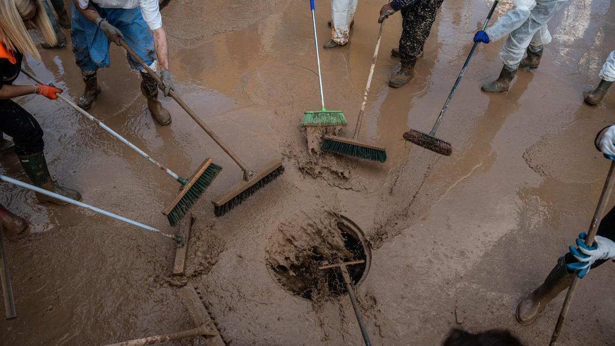 Varias personas retiran barro con cepillos en una alcantarilla de Alfafar