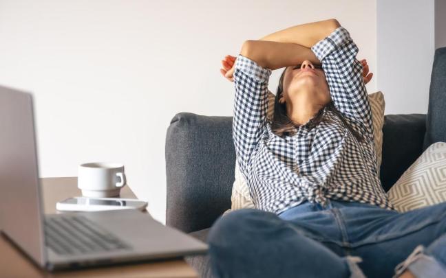 Una mujer agotada en el sofá junto a su portátil.