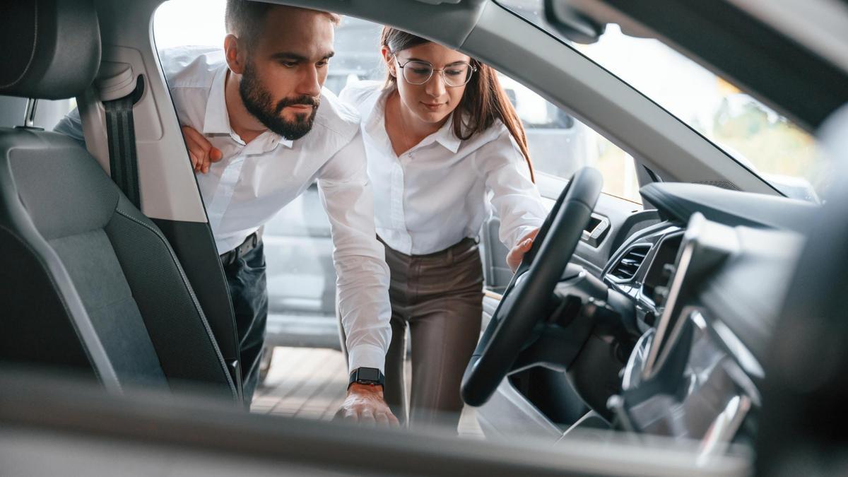 Dos personas miran el interior de un coche nuevo en un concesionario.
