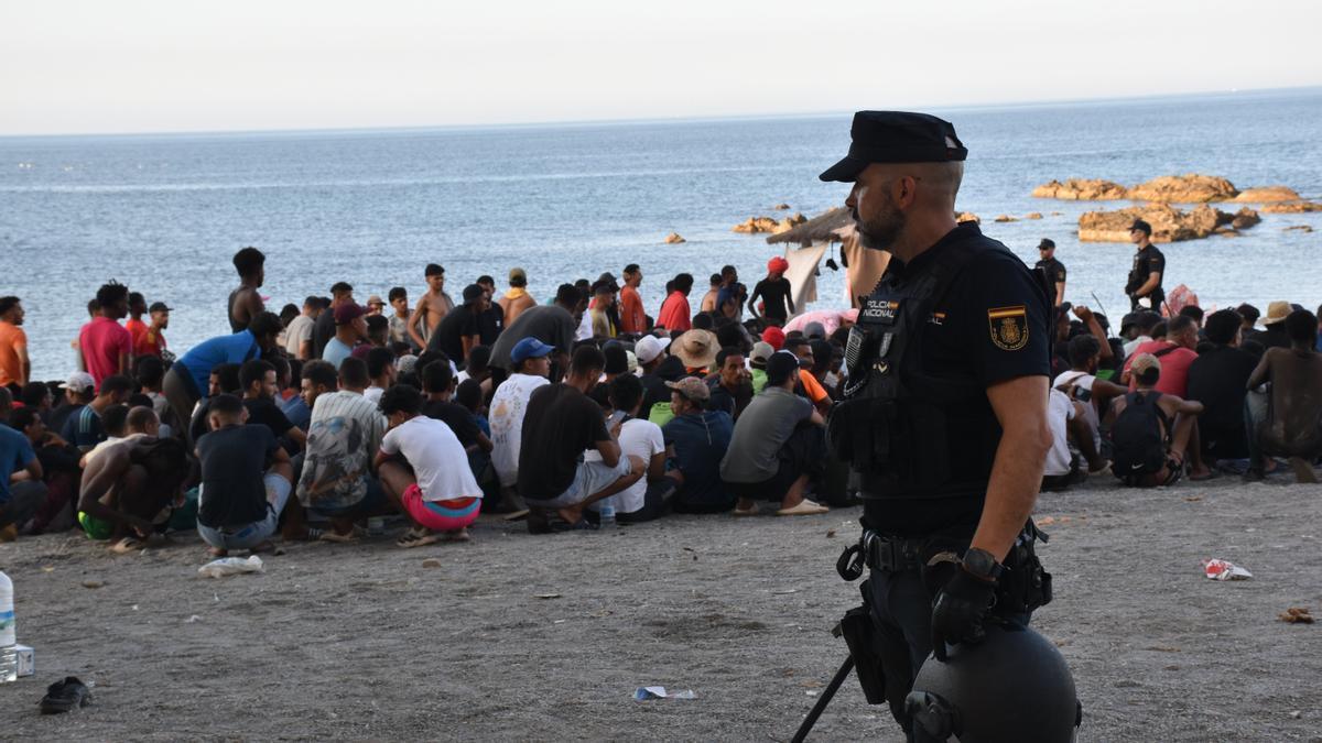 Un policía junto a decenas de migrantes en la costa de Ceuta.