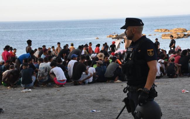 Un policía junto a decenas de migrantes en la costa de Ceuta.
