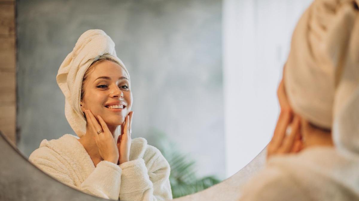 Chica se mira al espejo nada más salir de la ducha mientras se aplica sus cremas de cuidado facial.