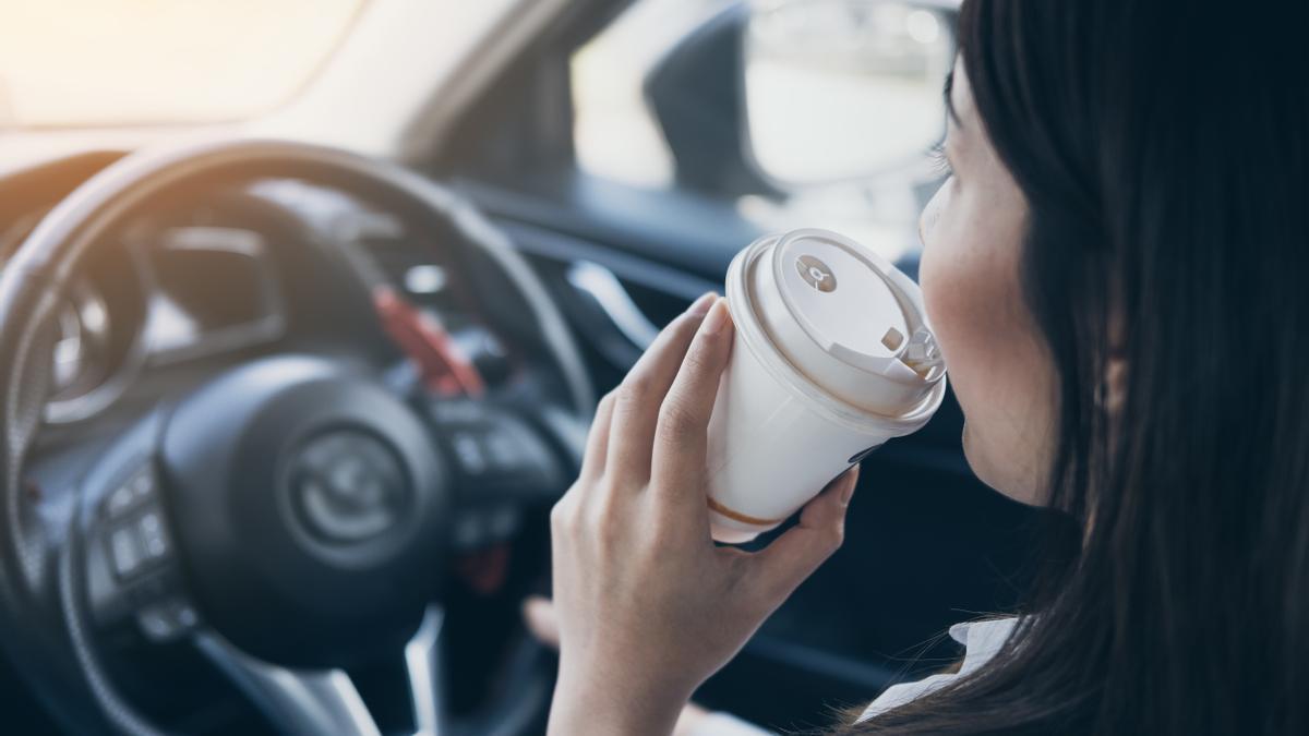 Una mujer se toma un café mientras conduce.