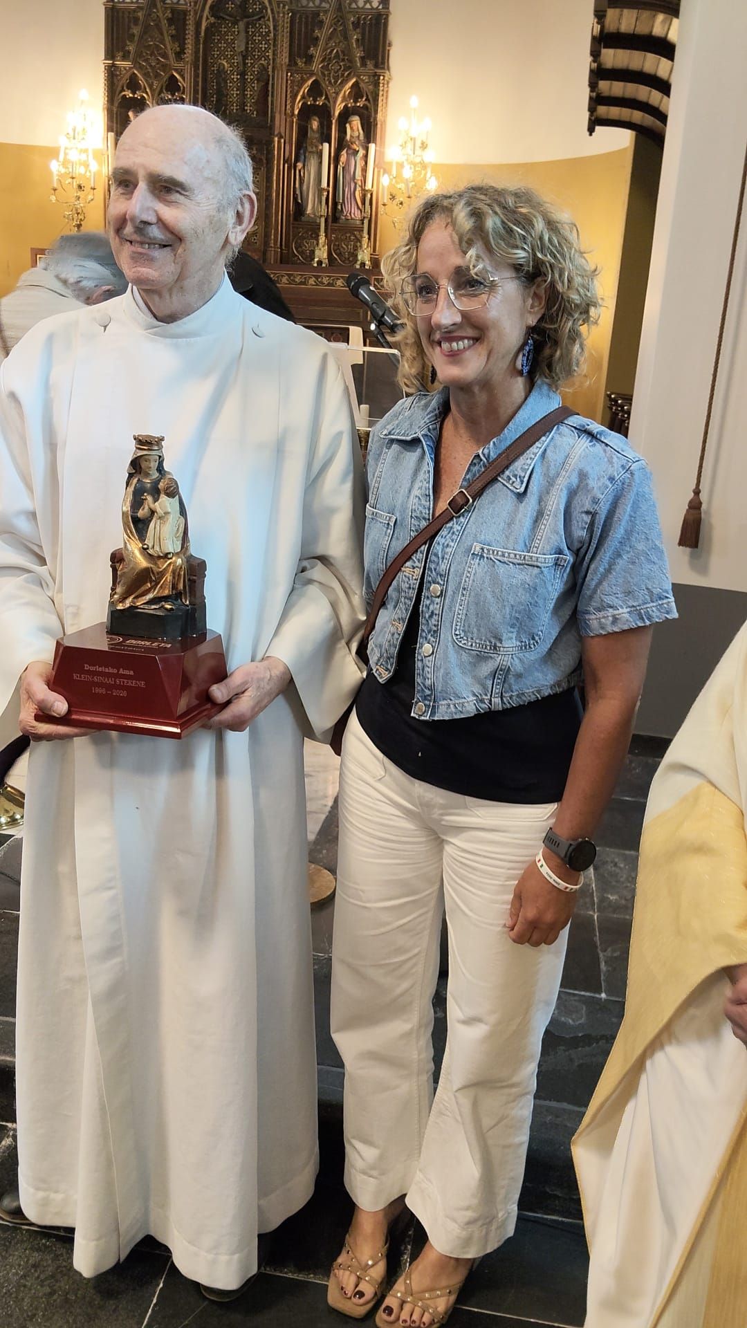 La alcaldesa gatzagarra hace entrega de una imagen de la Virgen de Dorleta al párroco de la iglesia de Saint-Eligius en Klein-Sinaai.
