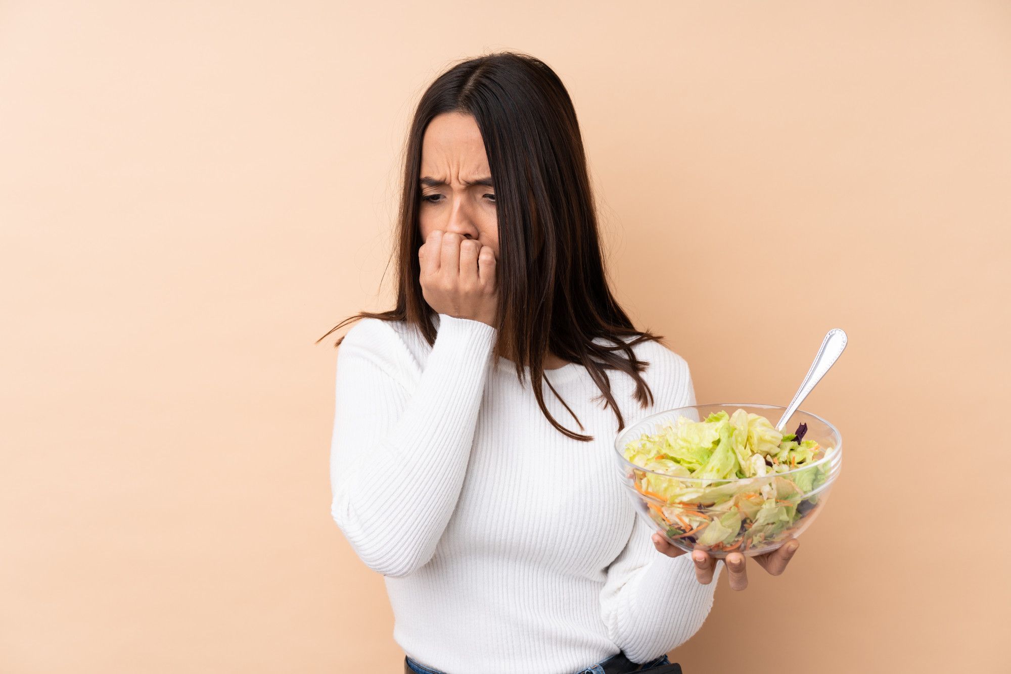 Una joven sujeta un bol con ensalada con cara de circunstancias.
