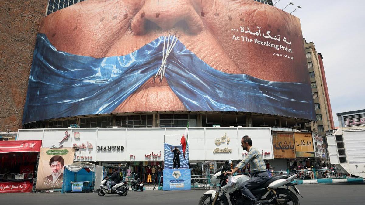 Ciudadanos iraníes circulan frente a una gran valla publicitaria antiestadounidense en la plaza Valiasr de Teherán, Irán.