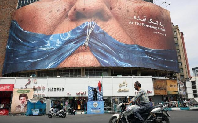Ciudadanos iraníes circulan frente a una gran valla publicitaria antiestadounidense en la plaza Valiasr de Teherán, Irán.