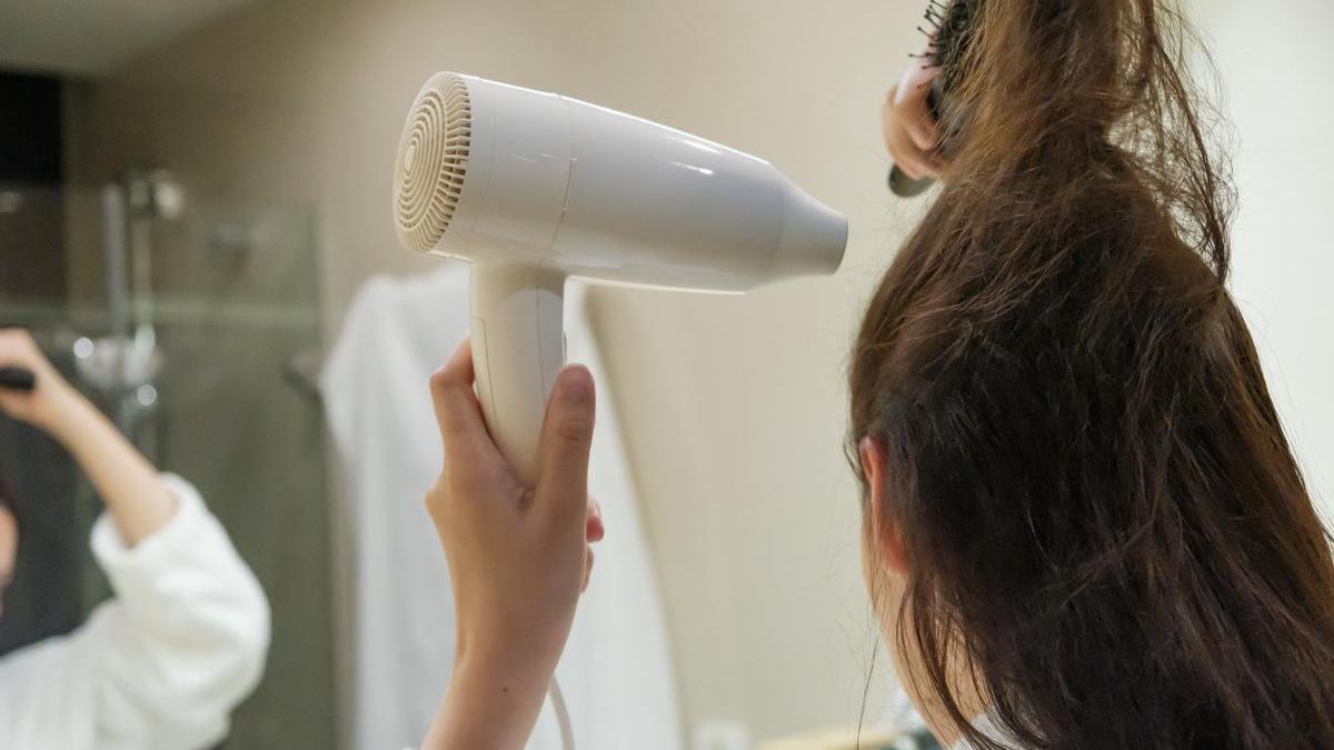 Mujer de espaldas se seca el pelo haciendo especial hincapié en las raíces.