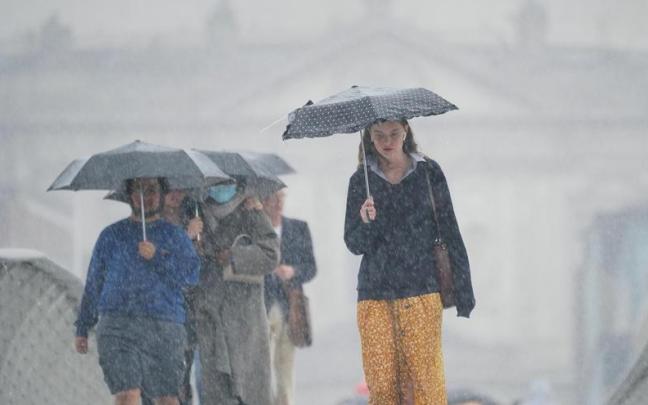Varias personas se refugian de una fuerte tormenta bajo sus paraguas.