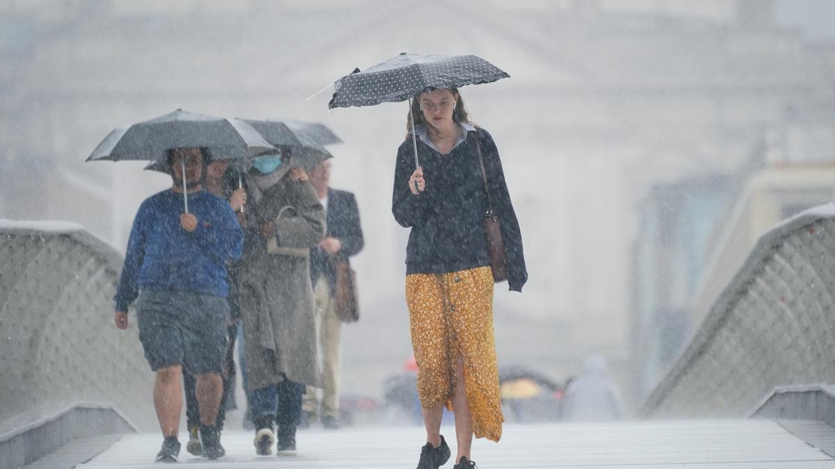 Varias personas se refugian de una fuerte tormenta bajo sus paraguas.