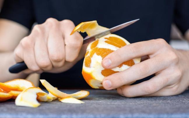 Manos de un hombre pelando una naranja.