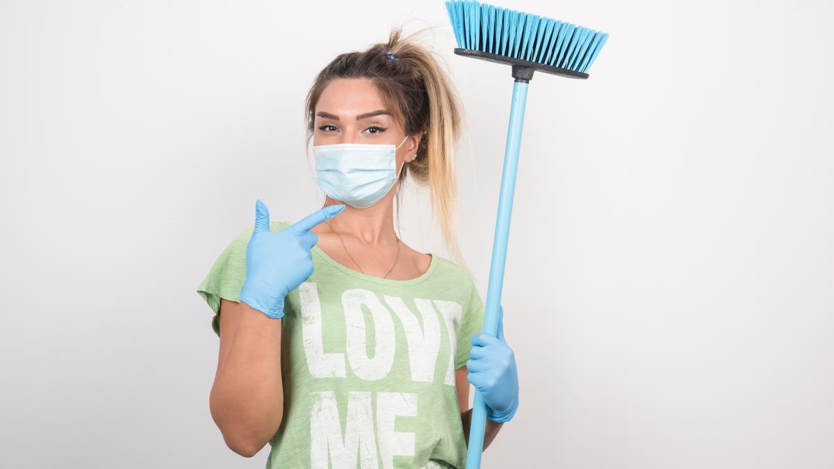 Mujer con mascarilla y guantes señalando a una escoba.